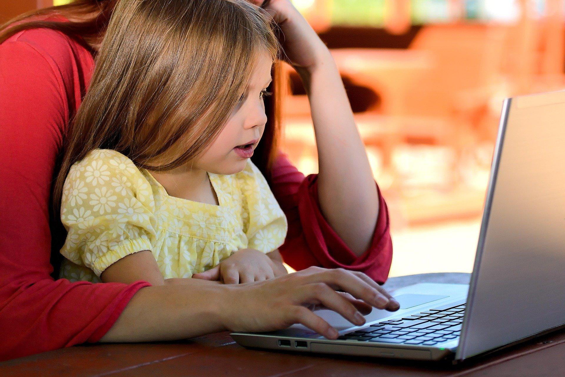 Niña y adulta frente a la pantalla de un portátil