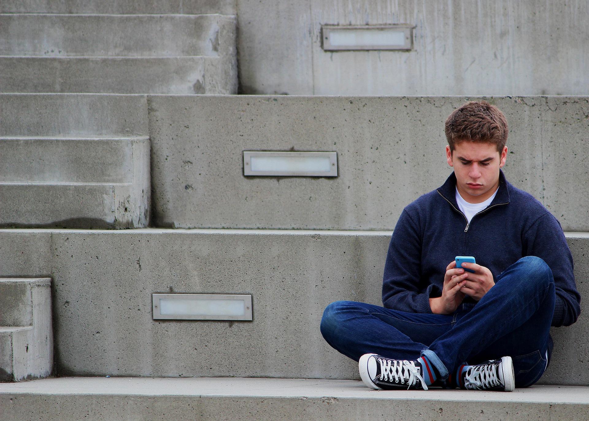 Adolescente con cara de preoucpación mirando el móvil en solitario